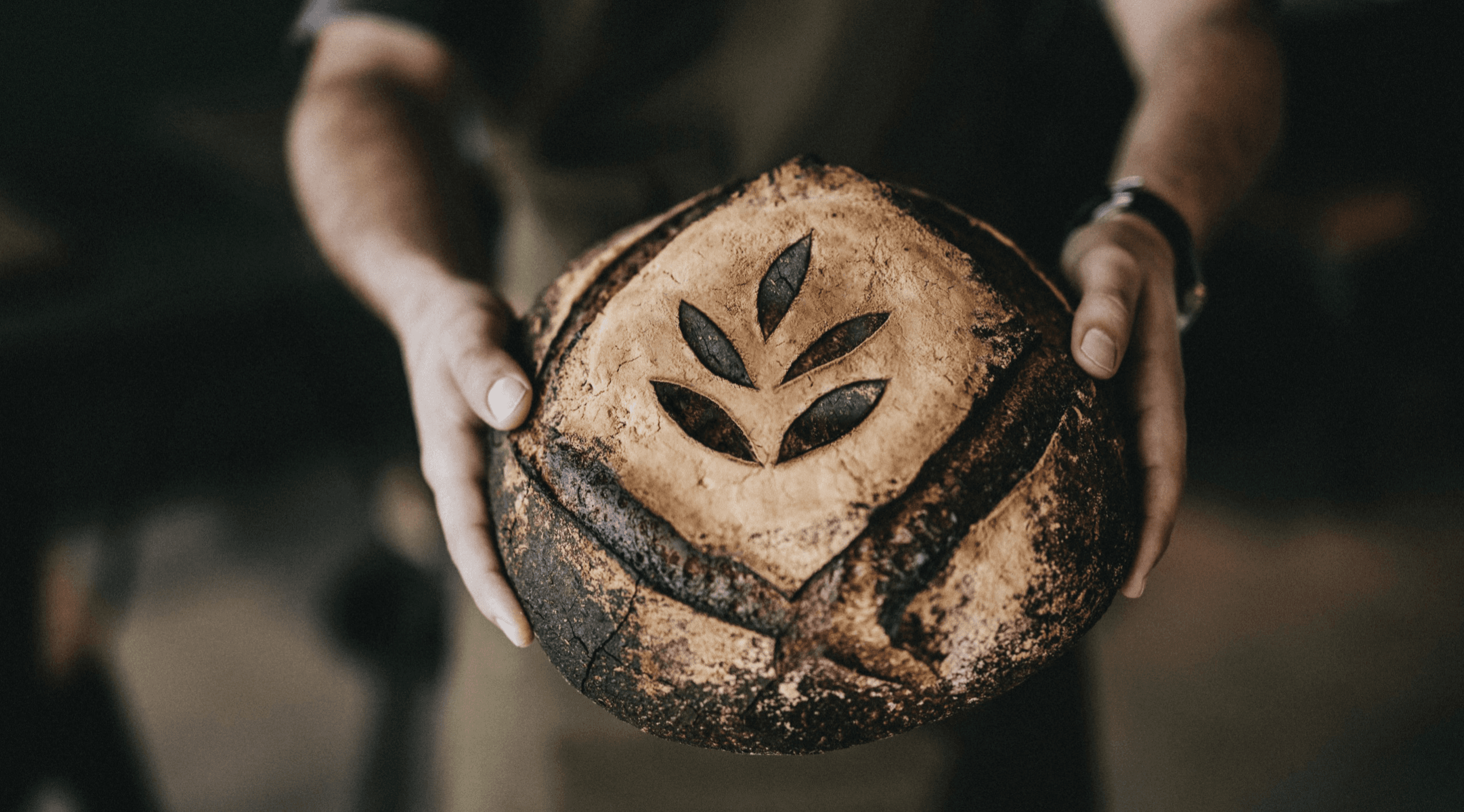 Baker holding a boule bread with the Guesa Trading SL logo embedded in it.